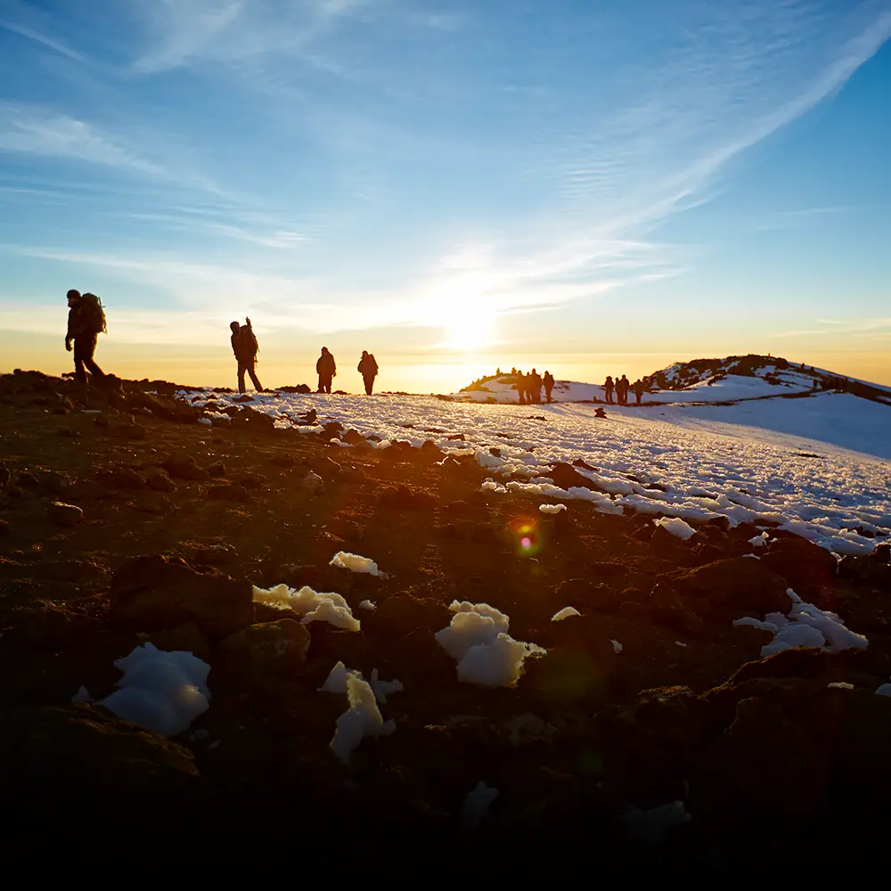 The sun just above the horizon with members of a expedition walking through snow
