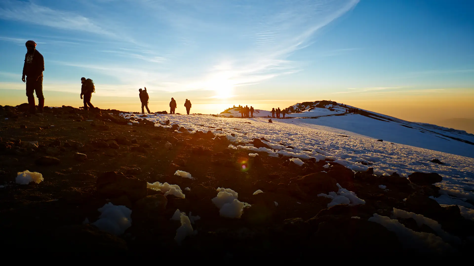 The sun just above the horizon with members of a expedition walking through snow