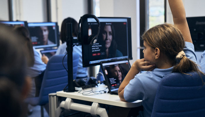 A student in a PSHE lesson with her hand up and the BecomingX Education platform on her computer screen.