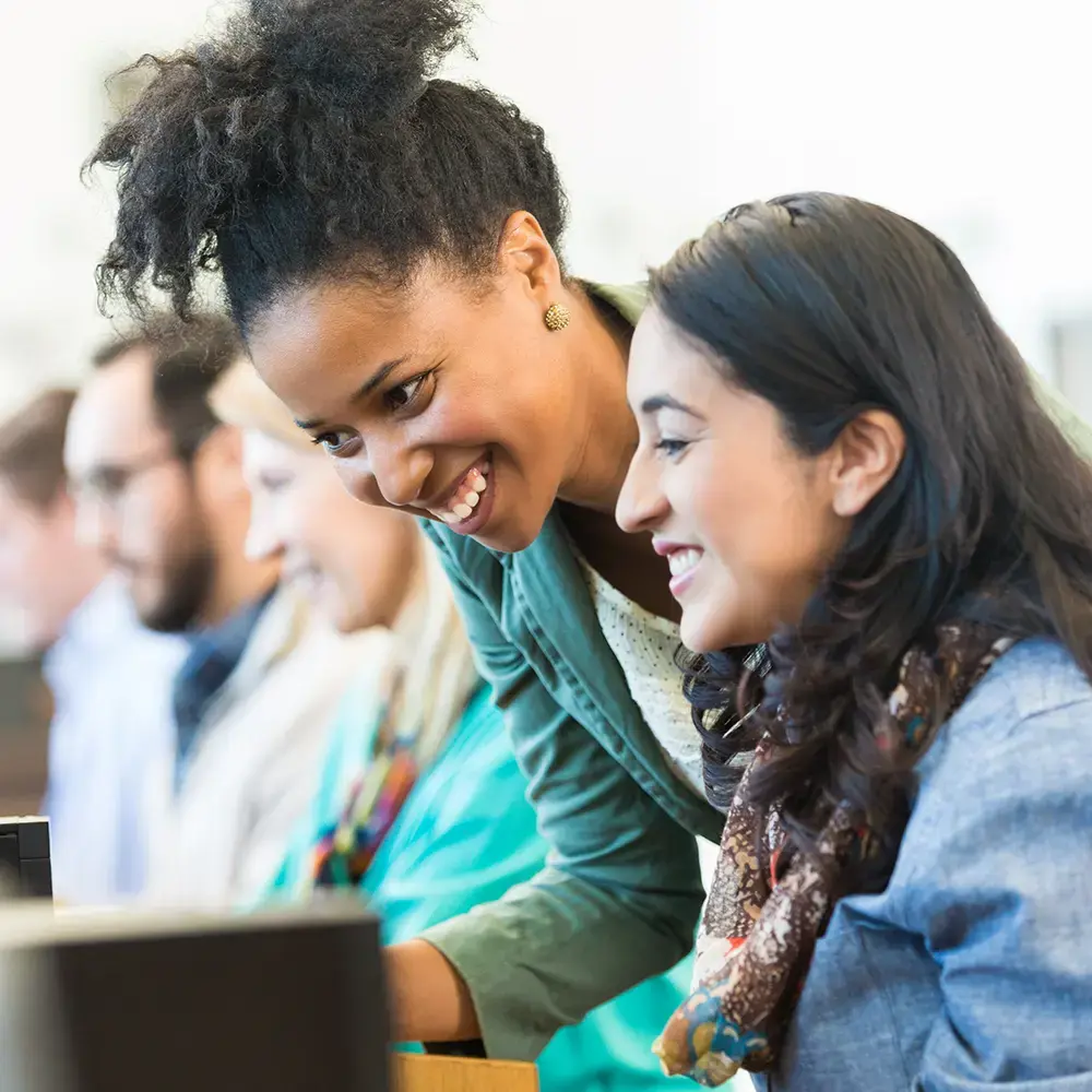 Two smiling females employees, one showing the other how to do a task