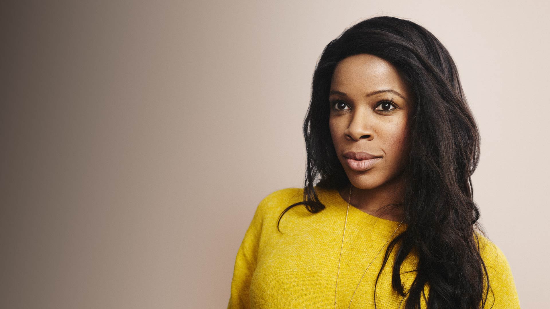 Portrait of a black female Accenture Managing Director wearing a yellow jumper.